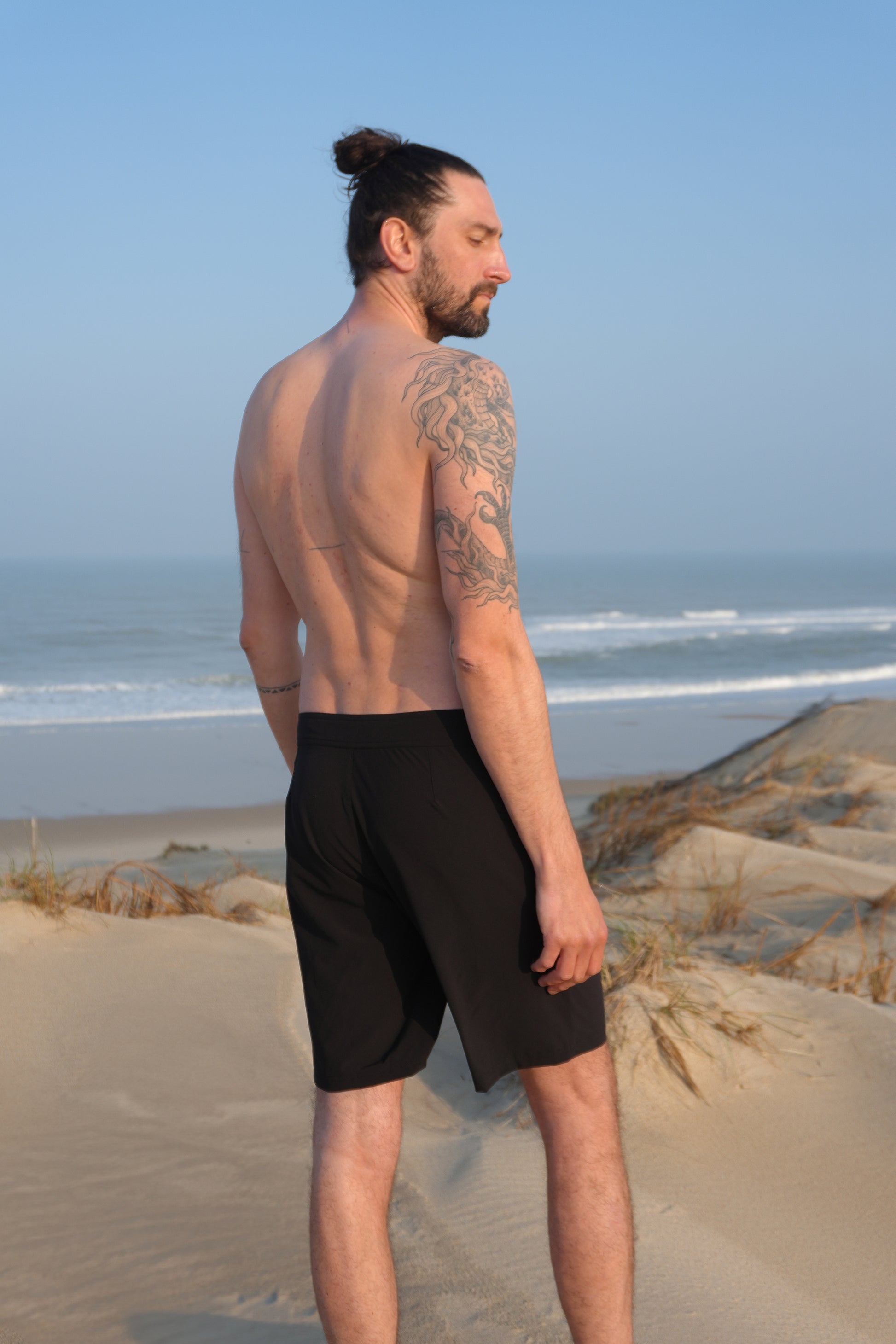 Model wearing AFATO boardshorts in black at the beach – designed for comfort, movement, and surf lifestyle performance.”