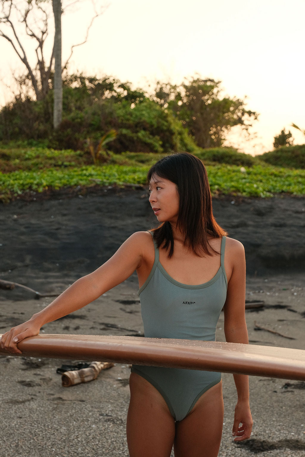 Model wearing AFATO Oceansuit in sage green holding a surfboard – capturing a relaxed and functional surf lifestyle.