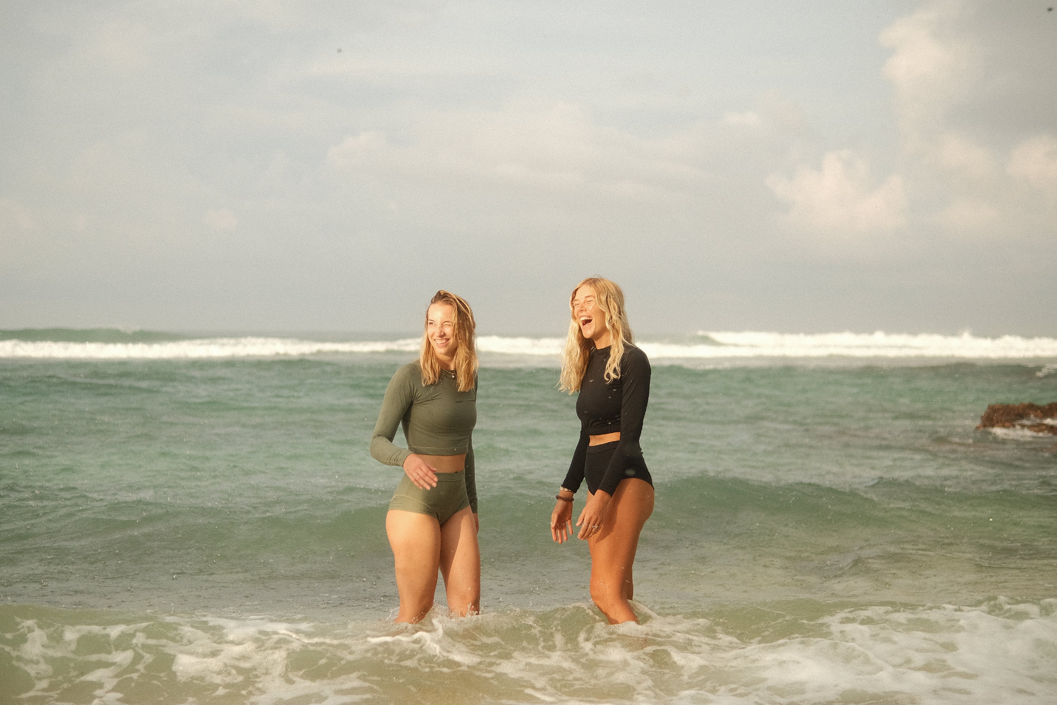 Two models wearing AFATO surfwear – one in sleek black, the other in calming sage green, perfect for beach days and surf sessions.