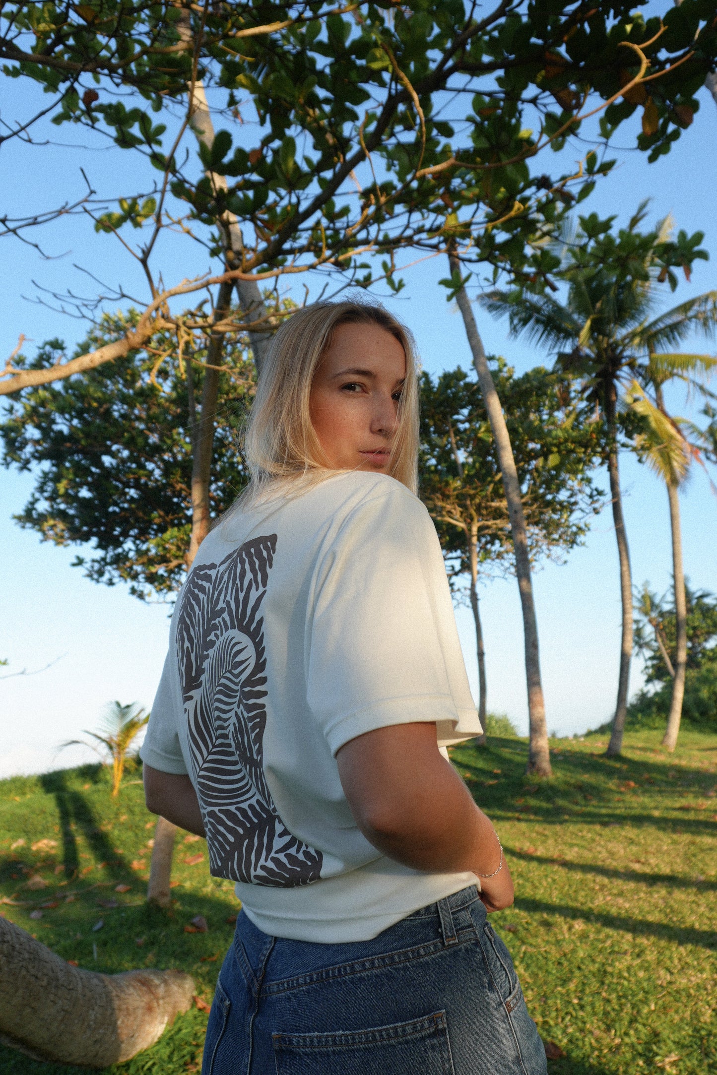 Female model wearing AFATO Palm Rhythm unisex shirt from the back – showcasing the relaxed fit and back print design inspired by palm and ocean rhythm.