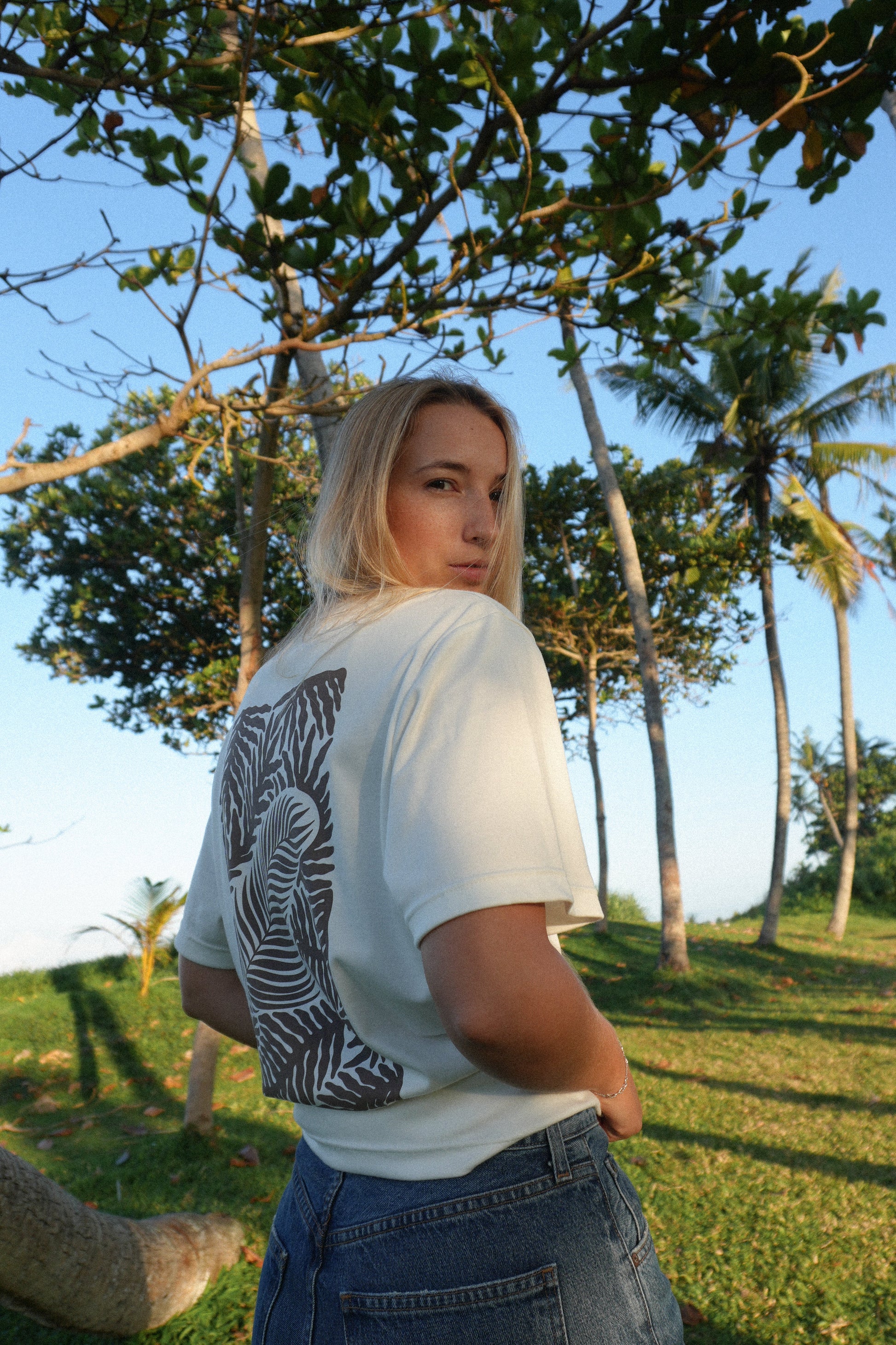 Female model wearing AFATO Palm Rhythm unisex shirt from the back – showcasing the relaxed fit and back print design inspired by palm and ocean rhythm.